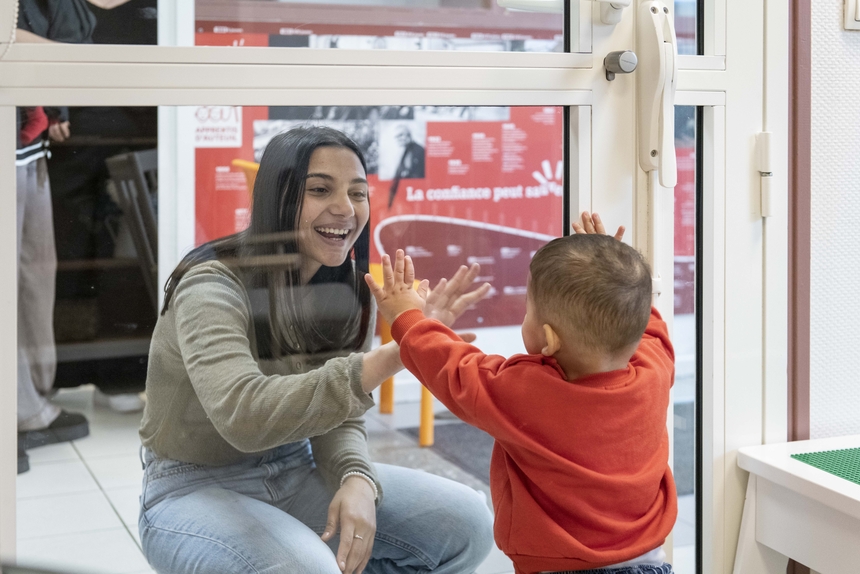 Une maman joue avec son petit garçon à travers une vitre.