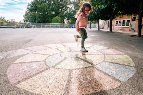 Une petite fille joue à la marelle dans une cour d'école