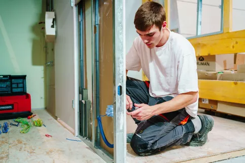 Un jeune homme travaille au sein d'un batiment en travaux, il s'occupe de l'électricité.