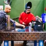 Un jeune homme porte des protections et s'apprête à faire de la soudure. Il est aidé par un professeur.